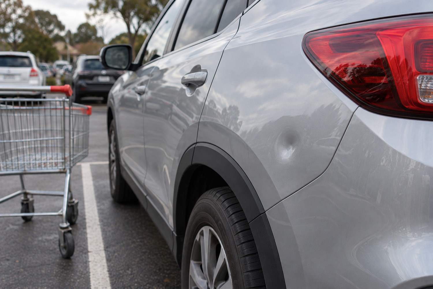Shopping trolley beside a shallow intact-paint dent on a silver SUV rear quarter
